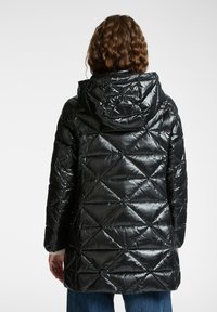 Zwarte pufferjack met een glanzende, gewatteerde textuur, voorzien van een capuchon, diagonale stiksels en elastische manchetten. De lengte reikt tot halverwege de dij.
