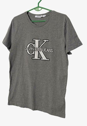 Camiseta de algodón gris con cuello redondo y mangas cortas, con un logotipo en blanco y negro de Calvin Klein Jeans impreso en la parte delantera.