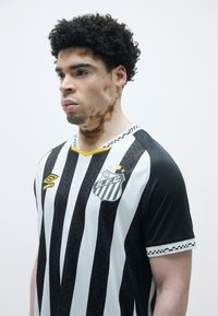 Svart og hvit stripete fotballtrøye med gul krage, med klubblogo og mønstrede detaljer på ermene.