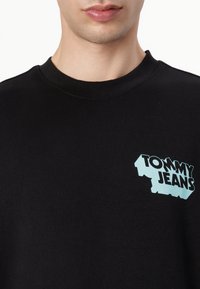 Zwarte sweatshirt met ribbelhals, voorzien van een turquoise grafische logo "TOMMY JEANS" op de linkerkant van de borst. Van katoen.
