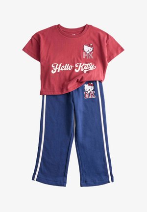 Maglietta rossa con stampa "Hello Kitty" e grafica del personaggio, abbinata a pantaloni blu con strisce laterali bianche e grafica coordinata.