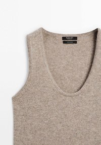 Lichtbruin cashmere tanktop met een diepe ronde halslijn, geribbeld trim en een zachte, textuurachtige oppervlakte. Label toont merk- en materiaaldetails.