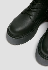 Czarne skórzane botki na kostkę z okrągłym noskiem, fakturowaną cholewką oraz grubą szarą gumową podeszwą z wyraźnym bieżnikiem.