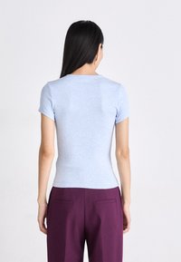 T-shirt azzurro chiaro aderente con maniche corte, realizzato in tessuto morbido e con una superficie liscia. Abbinato a pantaloni viola su misura.