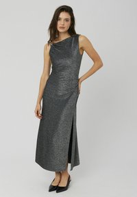 Robe maxi sans manches gris métallique avec une fente latérale et un détail froncé. Texture lisse, encolure asymétrique et un éclat subtil.