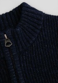 Granatowy sweter dzianinowy z wysokim prążkowanym kołnierzem, z metalowym zamkiem błyskawicznym z przodu i teksturowanym, miękkim materiałem.