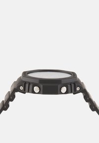 Orologio da polso analogico nero con cassa rotonda testurizzata, vetro trasparente, due pulsanti argentati e un cinturino flessibile e segmentato.