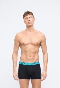Czarne bokserki z turkusowym pasem Nike. Materiał wydaje się gładki, z dopasowanym krojem i detalem otwarcia z przodu.