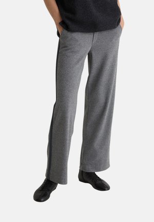 Pantalones gris de pierna ancha hechos de tela texturizada, con bolsillos laterales y costuras laterales negras en contraste, combinados con zapatos negros.