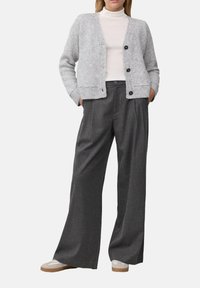 Grauer Strickcardigan mit V-Ausschnitt, Knopfverschluss und gerippten Bündchen, kombiniert mit hochtaillierten, weit geschnittenen grauen Hosen und beigen Schuhen.