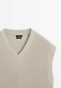 Pull sans manches beige en maille, avec un col en V, tissu texturé et finitions côtelées au niveau de l'encolure et des emmanchures.