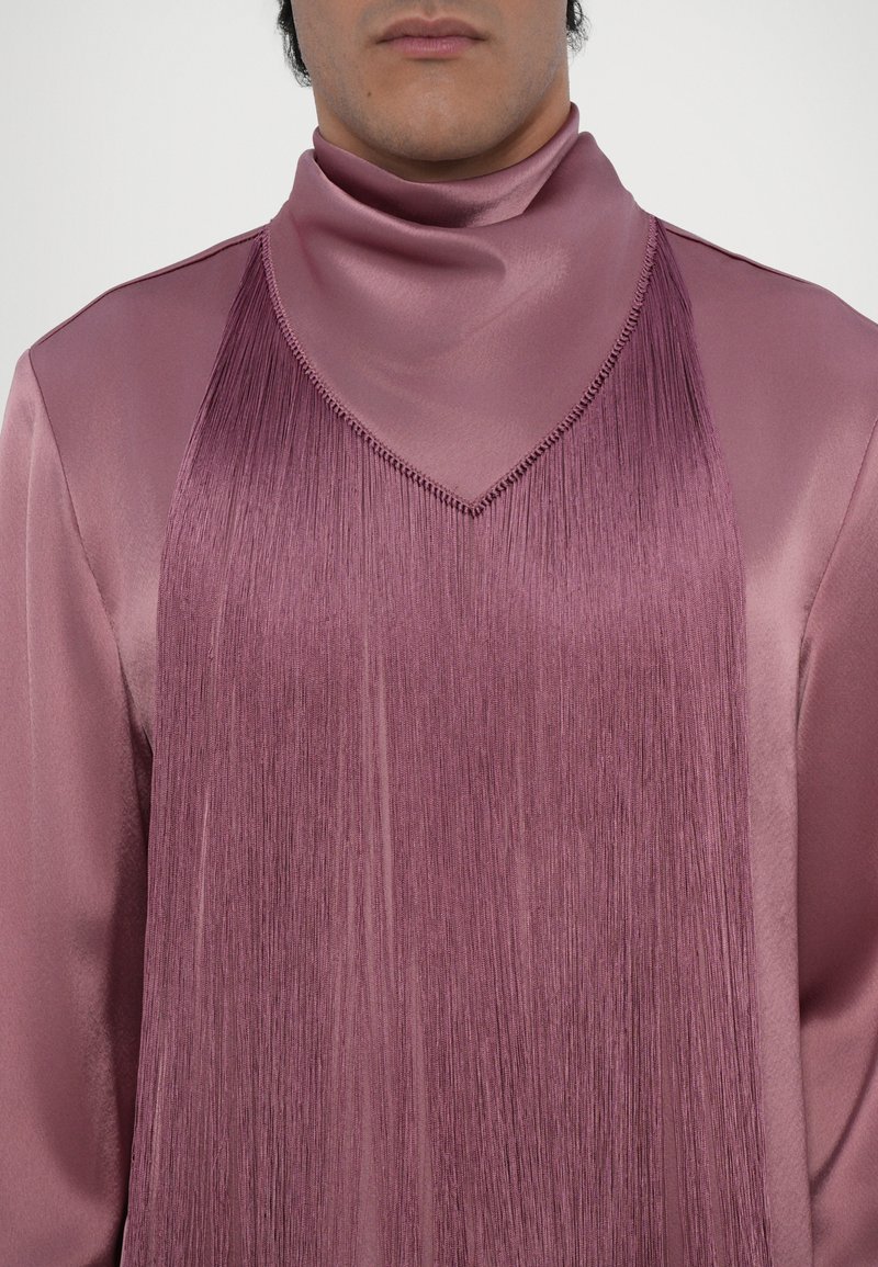 Vêtement en soie de couleur violet léger avec un col montant, présentant des détails de franges élaborés sur le devant et un décolleté en forme de V. Texture lisse.