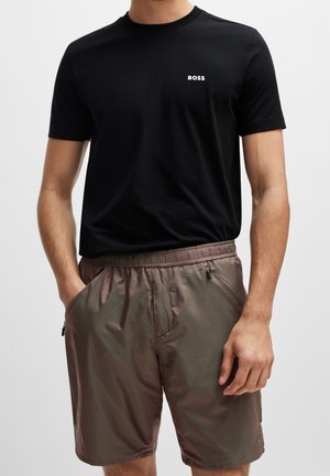 Schwarzes T-Shirt mit kurzen Ärmeln und weißem "BOSS"-Logo auf der Brust, kombiniert mit hellbraunen, leichten Shorts mit Seitentaschen.
