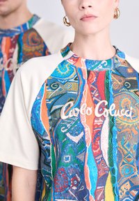 Flerfarvet kortærmet sweatshirt med livlige grafiske mønstre, hvide ærmer og "Carlo Colucci" broderet i midten.