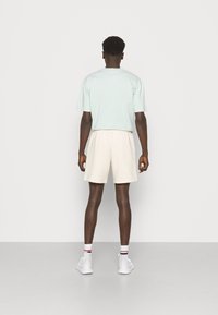 Miętowo-zielona koszulka z krótkim rękawem oraz kremowe szorty z elastycznym pasem. Ubranie uzupełnione białymi trampkami i paskowanymi skarpetkami do kostek.