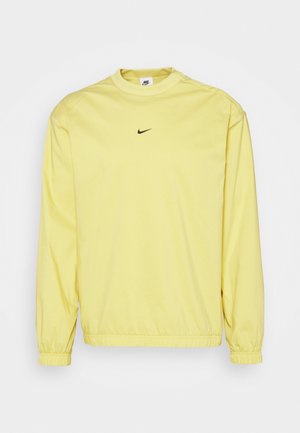 Sudadera Nike de manga larga de color amarillo claro con puños y bajo elásticos, con un pequeño logo negro de Nike swoosh centrado en el pecho.