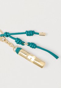 Avainketju, jossa on kiiltävä kultaiseen metalliin tehty koriste ja turkooseja nahkaisia yksityiskohtia, solmuvivahteita ja kiinnitysklipsi.