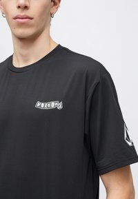 Μαύρο κοντομάνικο t-shirt από λείο ύφασμα με λευκό λογότυπο "Volcom" στο στήθος και αντίθετο σχέδιο στο μανίκι.