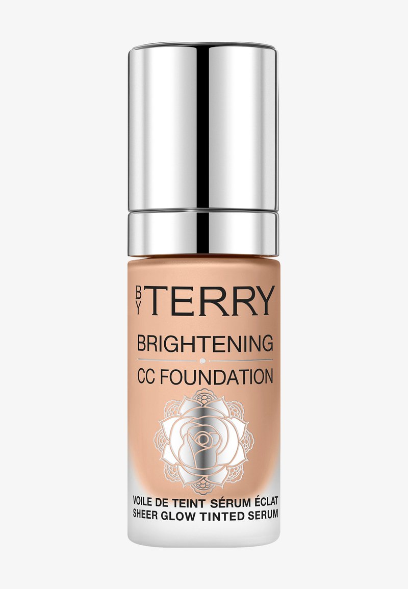 Fondotinta CC illuminante in una bottiglia di vetro satinato con pompa argentata. Presenta testo nero e un design di rose alla base. Colore beige chiaro.