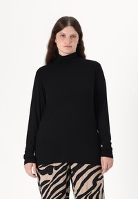 Svart langermet genser med høy hals laget av myk fabric, med en tettsittende design. Kombinert med beige bukser prydet med et svart zebramønster.