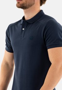 Polo de color azul marino con mangas cortas, que presenta un cuello clásico, una tapeta de tres botones y un sutil logo en el pecho.