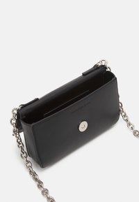 Borsa a tracolla nera Calvin Klein Jeans con tracolla a catena argentata e chiusura a scatto magnetico, mostrata aperta su uno sfondo bianco.