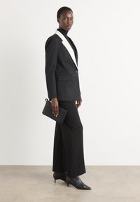 Black suit with a white shawl collar, layered over a black turtleneck. Paired with a black clutch and black pointed-toe heels. Smooth texture.