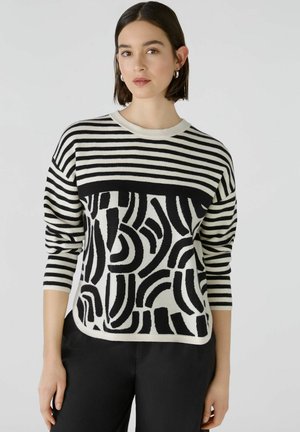 Schwarz-weißer Pullover mit horizontalen Streifen an den Ärmeln und einem geometrischen Muster am Körper. Weicher Strickstoff mit Rundhalsausschnitt.