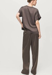 Bluza maro din satin cu mâneci scurte și croială lejeră, asortată cu pantaloni largi cu buzunare laterale și textură netedă.