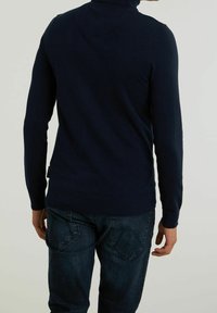 Mörkblå polotröja i stickad tyg, med långa ärmar och en figurnära passform, i kombination med mörka denimjeans.