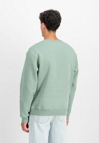 Miętowy sweatshirt z okrągłym dekoltem, ściągaczami przy mankietach i u dołu. Ma gładką teksturę i luźny krój, zestawiony z jasnymi dżinsami.