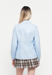 Camicia a maniche lunghe di colore blu chiaro con colletto e vita aderente, abbinata a una gonna a pieghe a scacchi. Presenta un tessuto morbido e un design strutturato.