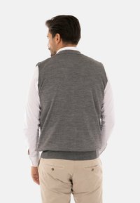 Gilet grigio a maglia con scollatura rotonda e orlo a coste, indossato sopra una camicia bianca. Design pulito senza motivo visibile o dettagli in metallo.
