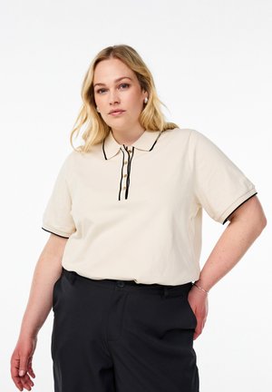 Beige pikétröja, kortärmad, med svart piping, knappslå med träknappar. Bärs med svarta byxor, smidig textur, avslappnad design.