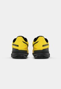 Baskets de sport jaune vif avec un dessus texturé, des accents noirs et une semelle en caoutchouc robuste avec un motif de traction distinct.