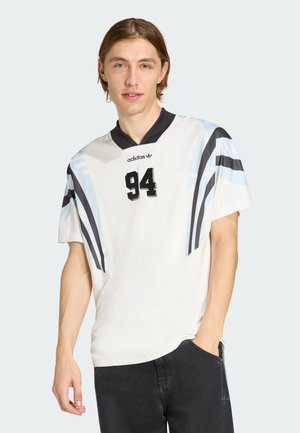 Maglia bianca a maniche corte con dettagli neri, strisce blu e numero 94 sul davanti. Presenta un classico colletto a V nero.