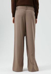 Lichtbruine wijde broek met een getailleerde pasvorm, voorzien van een gladde textuur, tailleband en twee achterzakken. Geen zichtbare sluitingen.