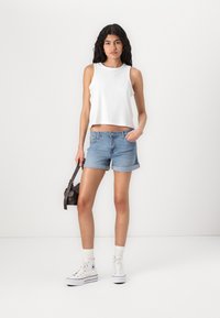 Vit, ärmlös croptop med ögonlocksstruktur; ljusblå denimshorts med uppvikta fållar; vita sneakers med grå detaljer; liten brun väska.