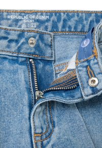 Light blue denim jeans with a zipper fly, featuring a silver button and contrast stitching. The waistband includes a label and a blue button.