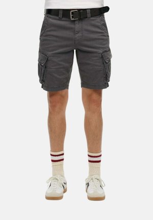 Man wearing dark grey cargo shorts with side pockets, a black belt, white sneakers, and cream socks with two red stripes.