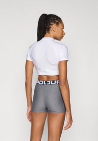 Λευκό κοντό αθλητικό τοπ με κοντά μανίκια συνδυασμένο με γκρι σορτς με υψηλή μέση που διαθέτει μαύρη μέση με το κείμενο «MOLDUR.»