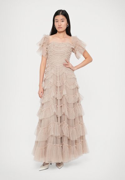 Pikk, kihiline kleit pehmes beežis tüllis, millel on volangiga detailid ja läbipaistvad puhvärvid. Omab istuvat bodi ja voolavat kihilist seelikut.