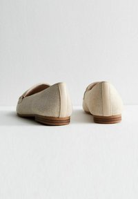 Zapatos casuales beige con upper de malla, punta redondeada y tacón bajo de madera. Presentan una parte posterior lisa y un sutil detalle de costuras.