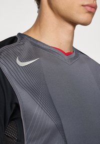Gray and black athletic jersey with a v-neck design, featuring a textured, ribbed pattern and a small silver Nike logo on the shoulder.