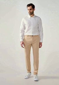Calças bege claro combinadas com uma camisa branca ajustada e sapatilhas brancas. O tecido parece suave com um corte reto.