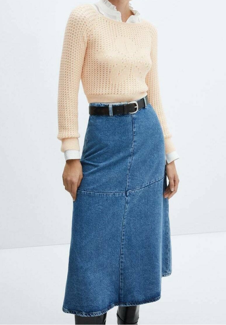 Pull en tricot pêche clair avec un motif floral, associé à une jupe en jean taille mi-haute de couleur bleue. Une ceinture noire cintrée à la taille, avec des poignets de chemise blanche.