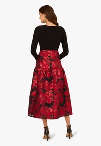 Schwarzes Korsettkleid mit einem voluminösen Rock aus rot-blümigem Muster. Der Stoff hat eine glänzende Textur und einen Reißverschluss auf der Rückseite.