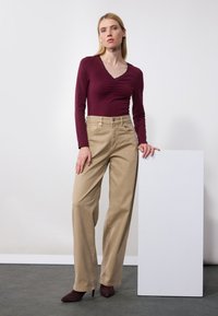 Burgundy long-sleeve top with ruched detailing paired with light beige wide-leg trousers, complemented by burgundy pointed heels.