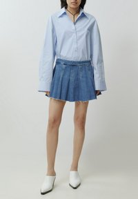 Lichtblauw button-up shirt met lange mouwen, gecombineerd met een denim geplooide rok met een onafgebroken zoom. Witte muiltjes met een spitse neus maken de outfit af.