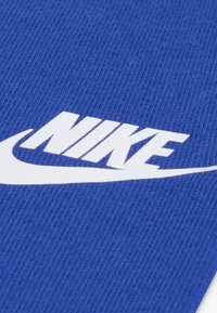 Blå strikket stof med et fremtrædende hvidt Nike-logo og swoosh-design. Teksturen er glat med en ribbet finish.